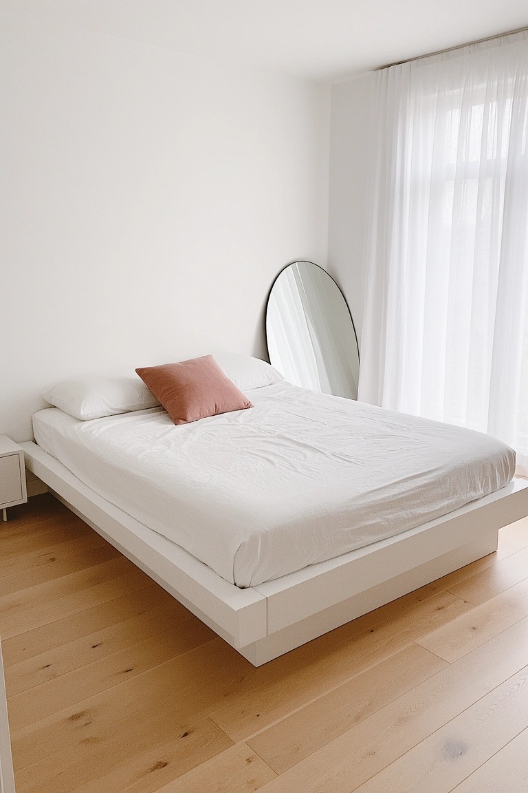 Bright white bedroom with platform bed on light wood floors, pink pillow accent, and arched floor mirror by window