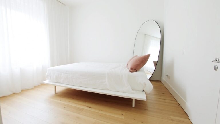 18 Bright Bedroom Color Schemes That Instantly Open Up Space Bright white bedroom with platform bed on light wood floors, pink pillow accent, and arched floor mirror by window