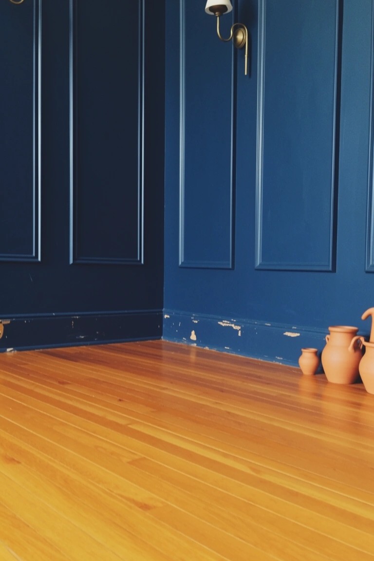 Deep navy paneled walls meeting warm wood floors with terracotta pots in a cozy bedroom corner