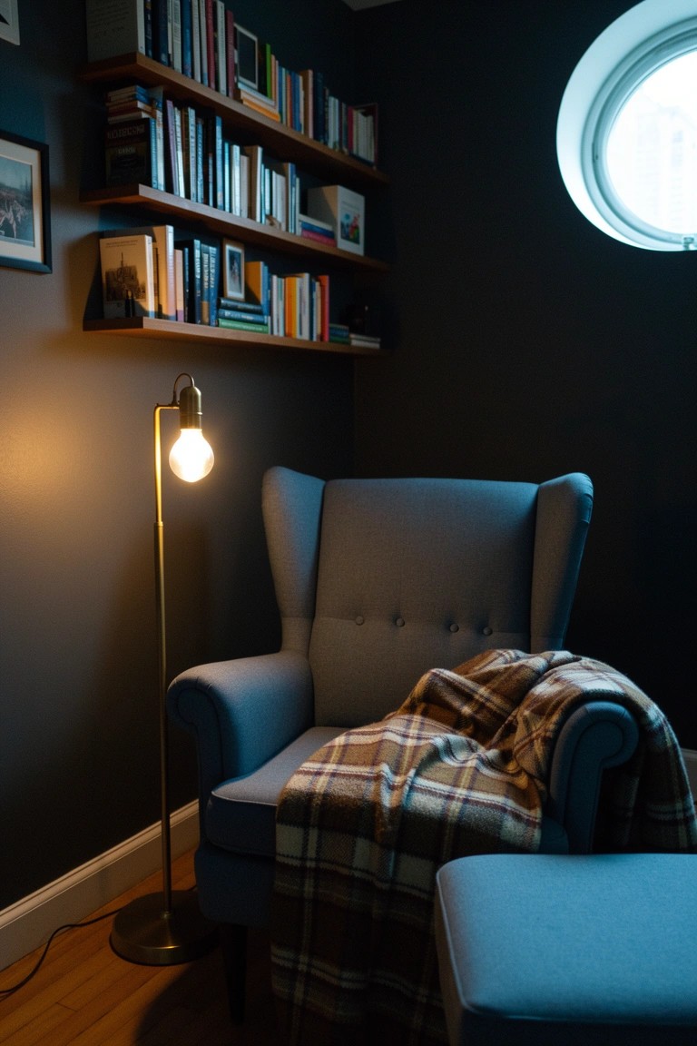 Cozy corner reading nook featuring blue wingback armchair with plaid blanket, wooden bookshelves, brass floor lamp, and round window in dark-walled room