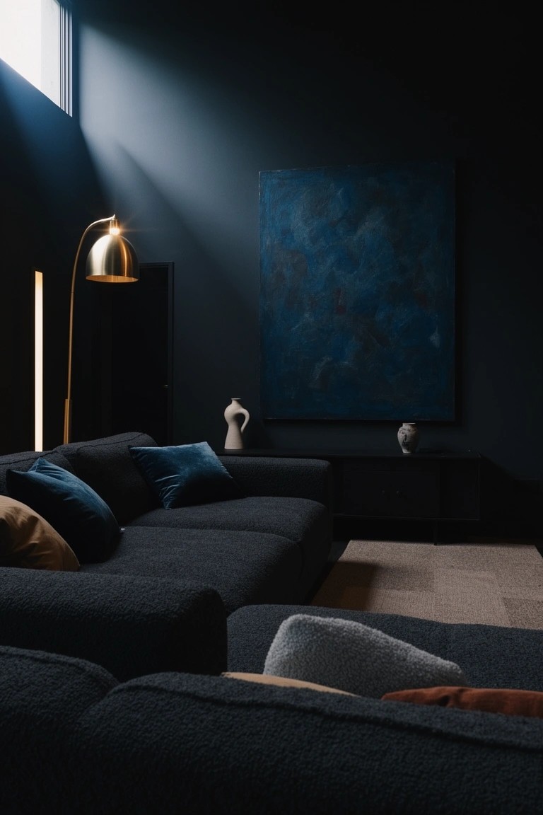 Modern living room with dark navy walls, black plush sectional sofa topped with colorful pillows, large abstract blue painting, gold arched floor lamp, and ceramic vases on black sideboard