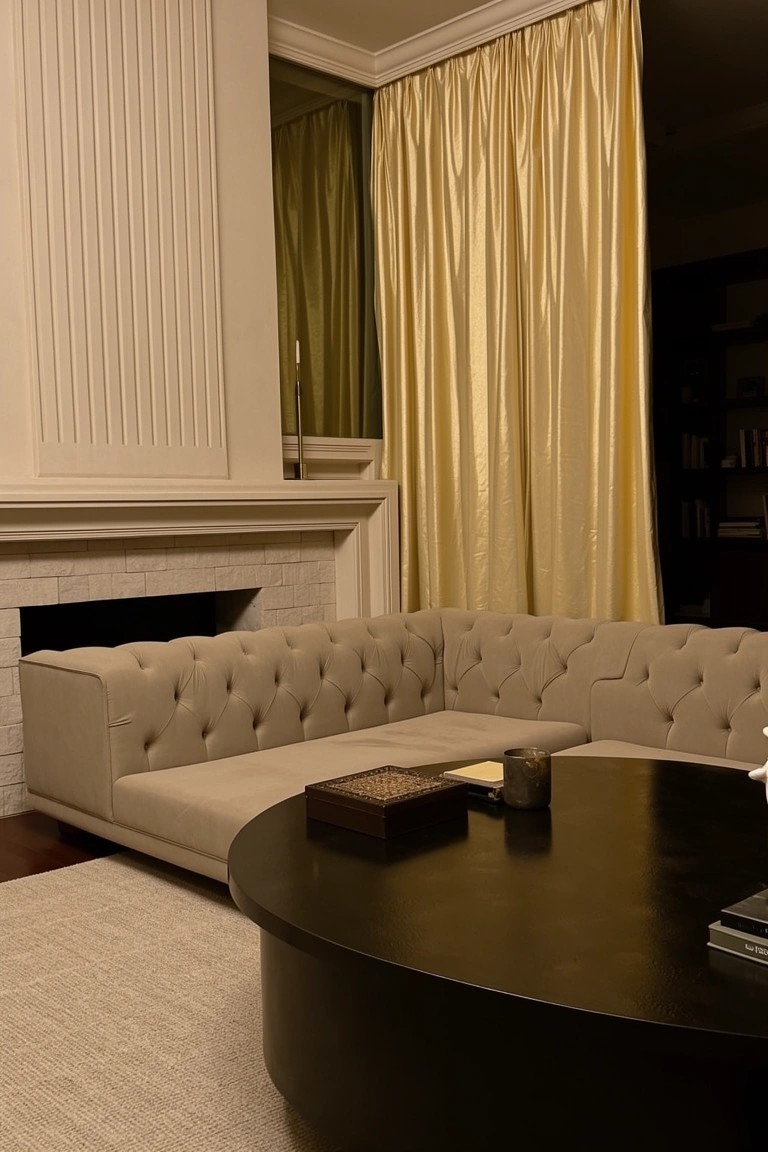 Neutral tufted L-shaped sofa facing brick fireplace with round black coffee table on beige rug