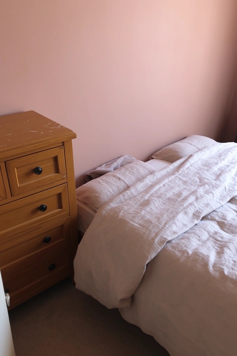 Serene bedroom with pale blush pink walls, wooden dresser, and white linens for a calm sleep space