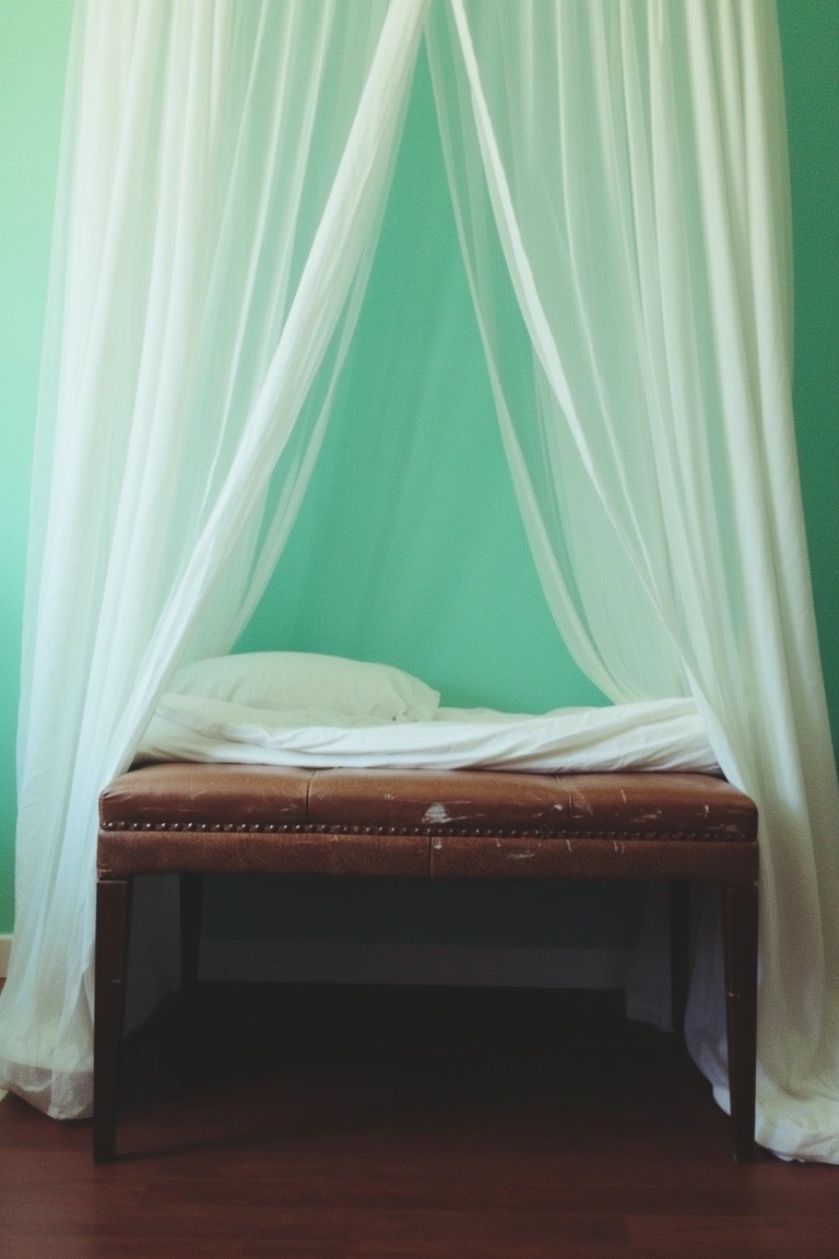 Pale mint green walls framing a simple bed with white canopy drapes and brown leather bench