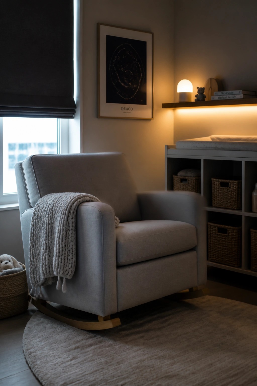 A light gray upholstered rocking chair with a wooden base and a chunky knit throw sits on a round rug in a neutral room with a framed star map on the wall.